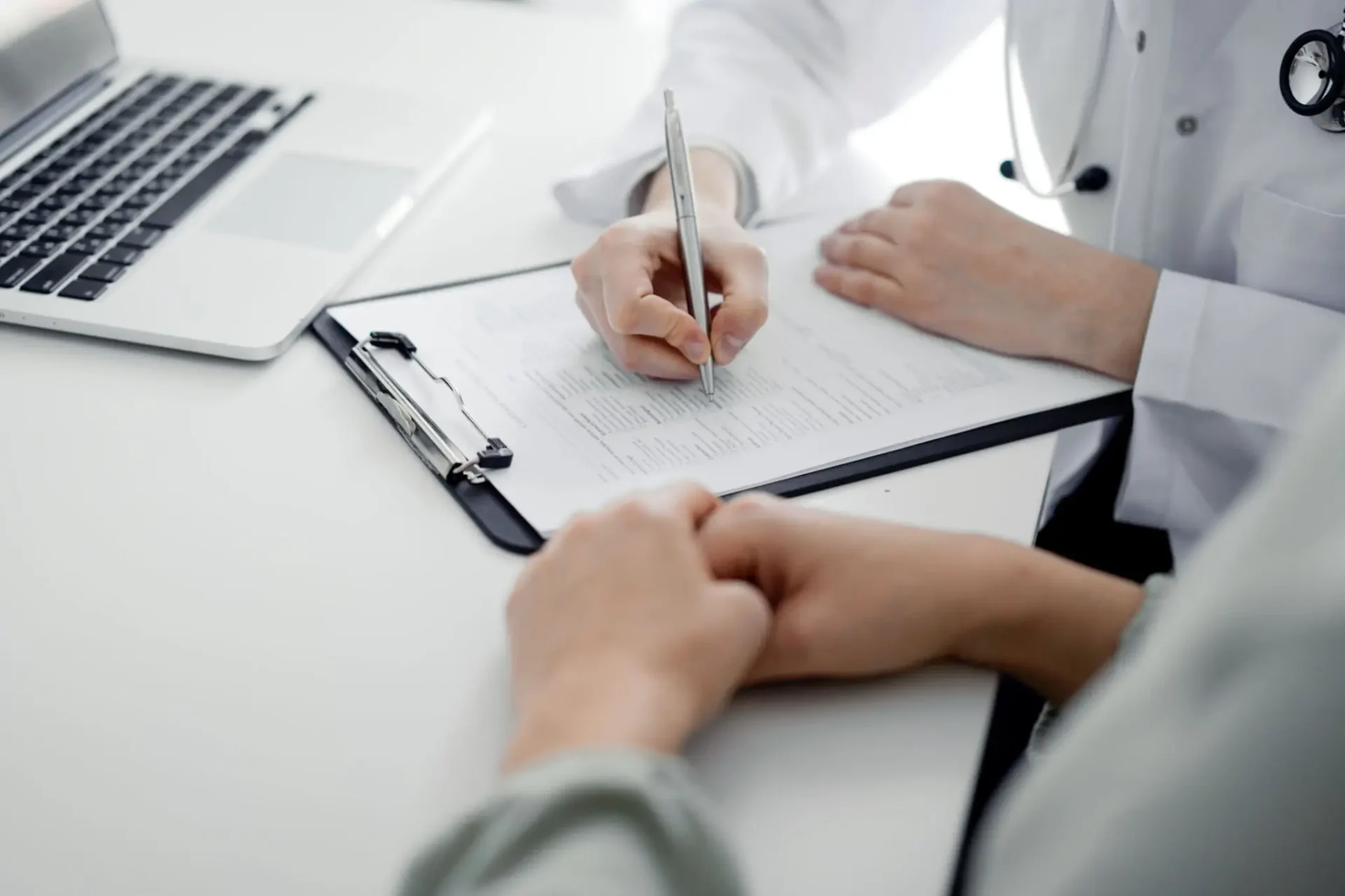 A person signing a document while another person watches.